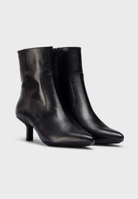 Botas de cuero negro hasta el tobillo con puntera afilada, tacones delgados y una cremallera lateral. La textura suave y el diseño ajustado realzan la apariencia elegante.