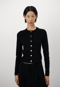 Svart strikket cardigan med lange ermer og rund hals, med gullfargede knapper foran og en cropped design.
