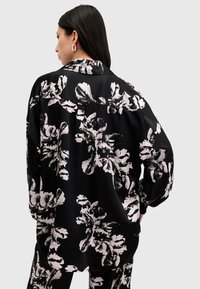 Blusa negra con estampado floral que presenta grandes patrones de flores blancas y rosas, fabricada en un tejido suave, de corte holgado y con cuello.