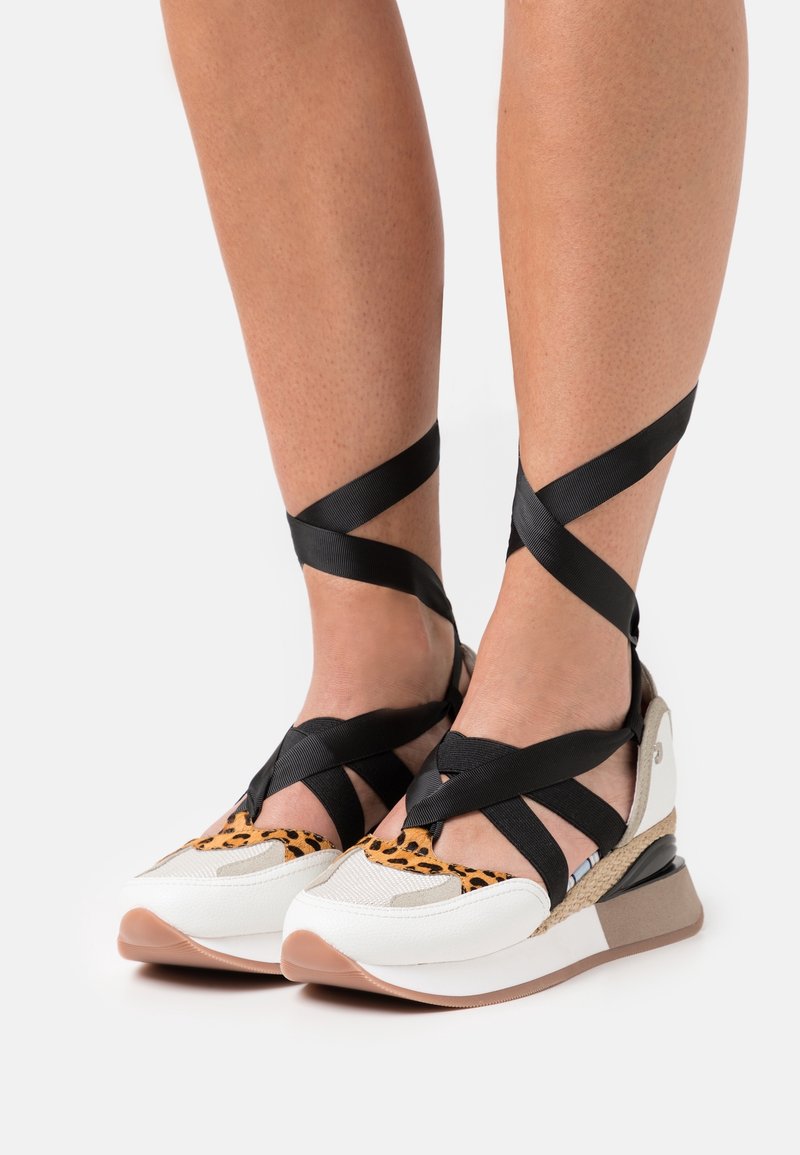 Sportovní boty s bílým a béžovým základem, akcenty s leopardím potiskem a černými textilními pásky křížícími se kolem kotníků. Gumová podrážka.