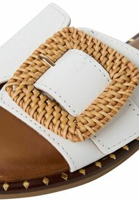Sandale à glissièren en cuir blanc avec une boucle tressée beige et une semelle intérieure marron, ornée de clous dorés sur la semelle extérieure.