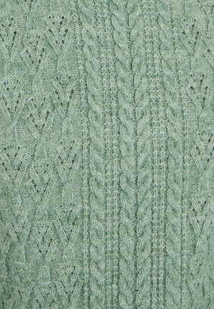 Tessuto lavorato a maglia verde chiaro con motivo di cuciture complesse, inclusi cavi e design a rete, che creano un effetto testurizzato e stratificato.