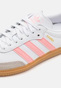 Weißer Ledersneaker mit pinken Streifen und goldenem "SAMBA"-Schriftzug. Verfügt über eine graue Wildleder-Frontakzentuierung und eine Gummisohle in Kaugummi-Optik mit strukturiertem Muster.