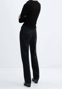 Jeans de mezclilla negra con un corte recto, que cuentan con bolsillos traseros y detalles de costura sutiles. Llevados con una camiseta de manga larga negra.