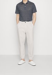 Polo de rayas en azul marino y blanco con cuello, combinado con pantalones de cintura elástica en beige. Zapatillas blancas sin cordones completan el atuendo.