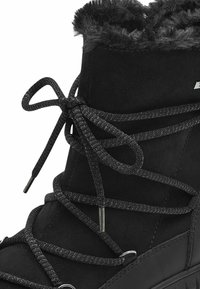 Botte en faux daim noir avec une texture duveteuse autour de la cheville, des lacets sombres et des œillets en métal pour un maintien sécurisé. Semelle plate.