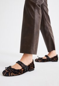 Zapatos planos de estampado de leopardo hechos de un tejido suave, con una correa negra con hebillas y un detalle de lazo en la parte frontal. Diseño de suela plana.