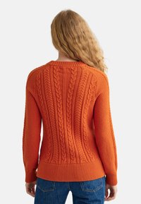 Pull en maille orange avec motifs torsadés texturés, poignets et ourlet côtelés. Tricot lisse sur le corps et coupe légèrement ample.
