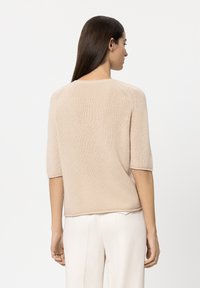 Light beige short-sleeve sweater with a soft texture, featuring a rounded neckline and subtle detail at the shoulder seams.