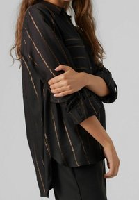 Black blouse with bronze vertical stripes, lightweight fabric, button-down design, long sleeves rolled at the cuffs, side slits at the hem.