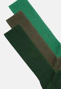 Drei Paar gerippte Socken in unterschiedlichen Grüntönen: dunkelgrün, gedecktes Oliv und leuchtendes Teal, mit einer glatten Textur und geradem Schnitt.