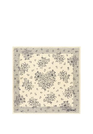 Pañuelo cuadrado beige con patrones florales y de hojas negras y un borde decorativo, mostrando una pequeña etiqueta con el nombre de la marca.