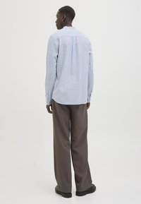 Cămașă albastră deschis cu mâneci lungi și croială relaxată, cu manșete cu nasturi și tiv drept, purtată împreună cu pantaloni întunecati, cu croială largă și pantofi negri.