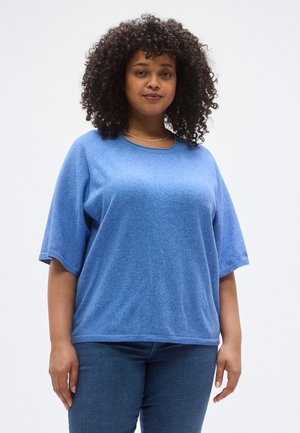 Haut tricoté bleu à manches courtes avec un col rond et une coupe décontractée. Texture lisse et motif chiné subtil. Porté avec un jean en denim.