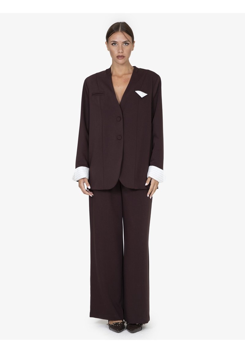 Bruine op maat gemaakte blazer met één knoop, brede mouwen en een witte zakdetail. Gepaard met bijpassende brede broek en puntige schoenen.