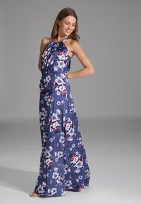 Robe maxi florale en navy, avec un col halter, un buste ample, et une jupe fluide ornée d'un mélange de fleurs blanches et bordeaux.