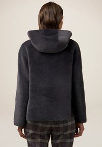 Chaqueta de piel de color gris oscuro, texturizada, con capucha y corte relajado; combinada con unos pantalones de cuadros.