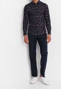 Navy floral printed button-up shirt with long sleeves, paired with tailored dark pants and white sneakers. The shirt features a spread collar.