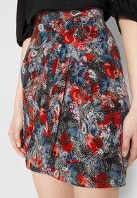 Gonna plissettata floreale con sfondo nero e intricati motivi paisley e fiori in rosso, blu e bianco, realizzata in tessuto leggero.