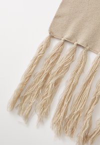 Tissu tissé beige avec des détails en franges à une extrémité. Les franges sont longues et texturées, ajoutant un intérêt visuel au design.