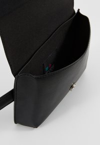 Sac à main en cuir noir avec une texture lisse, doté d'une fermeture à bouton-pression, d'un intérieur ouvert et d'une étiquette de marque visible à l'intérieur.
