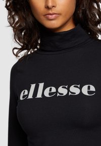 Juodas golfas su lygiu paviršiumi, ant krūtinės išryškinta žodžiu "ellesse" drąsiais baltais rašmenimis. Artimas vaizdas.