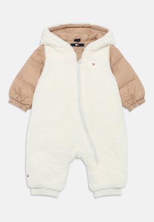 Hvit fleece heldrakt med beige quiltede ermer og hette, med en frontglidelås og logo-lapp på brystet.