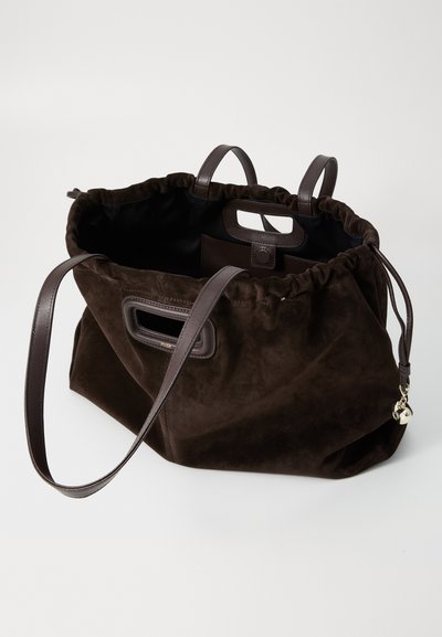 Brown suede tote bag with gathered top, dual leather handles, interior pocket, and a small gold charm attached. Smooth texture and soft appearance.