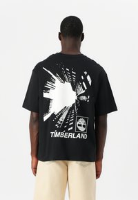 Svart bomull t-skjorte med et grafisk trykk av abstrakte bylandskaplinjer og "TIMBERLAND"-logoen i hvitt på baksiden.