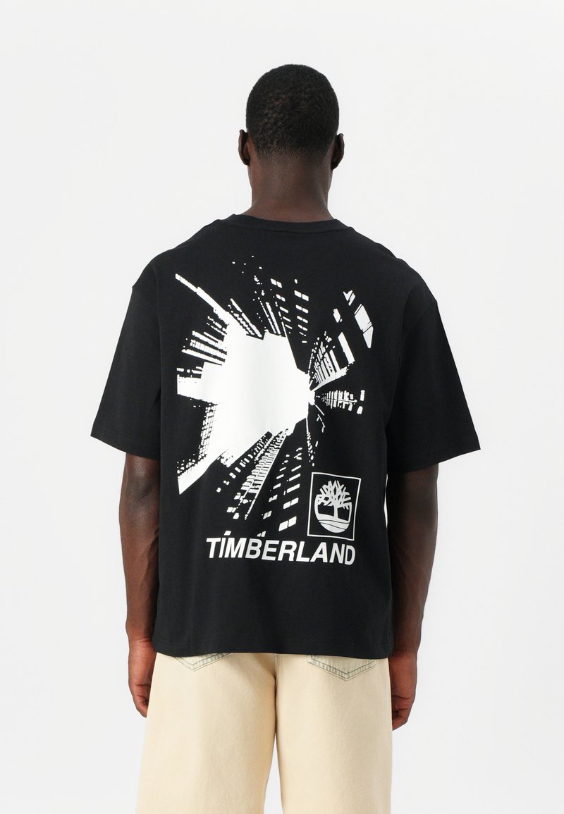 Svart bomull t-skjorte med et grafisk trykk av abstrakte bylandskaplinjer og "TIMBERLAND"-logoen i hvitt på baksiden.