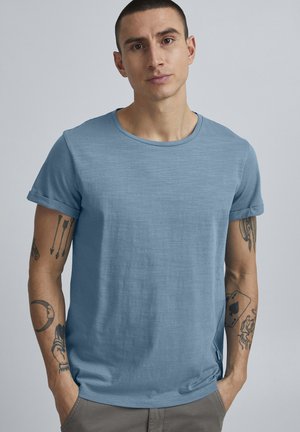 Lyseblå T-shirt med rund hals og oprullede korte ærmer. Lavet af blødt tekstureret stof, med sidespalter i kanten. Casual pasform.