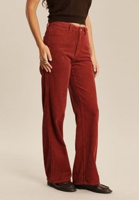 Pantalons en velours côtelé rouge à jambes larges, avec un côtelage vertical, taille haute et poches avant. Associés à des chaussures noires et un haut ajusté.