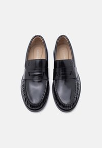 Paire de mocassins noirs en cuir sans lacets avec coutures style mocassin et une large bande sur le dessus, marqués Calvin Klein à l'intérieur.