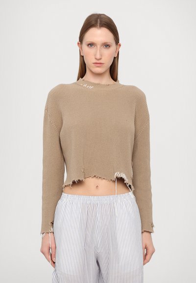 Pulover bej scurt, cu textură în fâșii, margini desfăcute și mâneci lungi. Asortat cu pantaloni deschiși cu dungi.