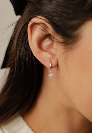 Pendiente de aro de plata con un colgante en forma de estrella que lleva pequeños cristales, colgando cerca del lóbulo de la oreja, mostrando un fino detalle y brillo.