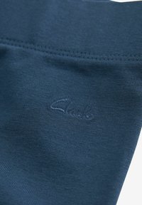 Tessuto blu navy con una texture liscia, caratterizzato da un logo sottile in basso a sinistra e un orlo cucito. Vista ravvicinata del materiale.