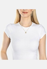 Collana d'oro con un piccolo pendente circolare, indossata sopra una t-shirt bianca aderente a maniche corte. Texture liscia e design semplice.