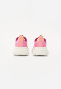 Sneakers atletiche rosa con un materiale testurizzato, caratterizzati da una suola bianca, strisce gialle e rosa sul retro e dettagli imbottiti sul tallone.