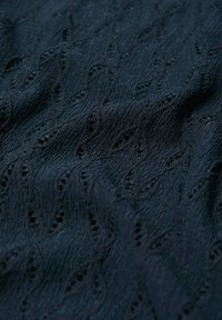 Tissu bleu marine foncé avec un motif de feuilles en relief texturé et de petits trous répartis sur toute la surface, créant un design délicat et complexe.