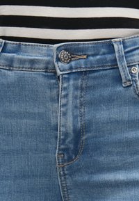 Hellblaue Denim-Jeans mit mittlerer Waschung, ausgestattet mit einem Metallknopf am Bund, sichtbaren Nähten und einer glatten Textur.