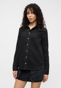 Μαύρο τζιν πουκάμισο με κουμπιά, με μυτερό γιακά, μακριά μανίκια και ασημένια κουμπιά, που διαθέτει καμπυλωτό τελείωμα και διακριτική ραφή.