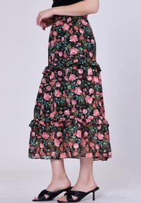 Jupe maxi florale avec un fond noir et des motifs floraux roses et verts, détail de volants superposés et tissu léger.