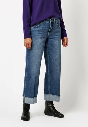 Wide-leg blue denim jeans with a frayed hem and contrasting light blue cuffs. Paired with black lace-up ankle boots.