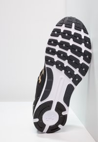 Semelle de chaussure de sport noire avec un design texturé, des accents blancs et un motif de traction sous le pied. Logo de marque bien visible.