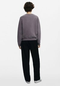 Halli puuvillane svettari, millel on ribidega mansetid ja äär, millele on sobitatud mustad lõdvad püksid. Disain sisaldab ümmargust kaelaauku ja minimaalset detailikäsitlust.