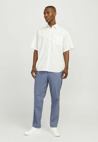Camisa de rayas blanca de manga corta con un bolsillo en el pecho, combinada con pantalones azules claros y zapatillas blancas. Diseño simple y informal.