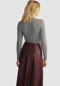 Długa bluzka z długimi rękawami w wzorzystym czarno-białym materiale, zestawiona z długą bordową skórzaną spódnicą. Gładka faktura i dopasowany krój.