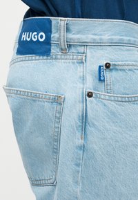 Ανοιχτό μπλε τζιν παντελόνι με πίσω τσέπη και μπλε ετικέτες με την επωνυμία HUGO κοντά στη μέση και την πλευρική τσέπη.