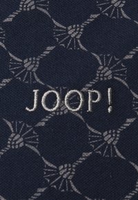 Tamsiai mėlyna medžiaga su pakartotu šviesiai pilku geometriniu raštu ir mazgų motyvais; siuvinėtas "JOOP!" logotipas sidabrinės spalvos siūlais.