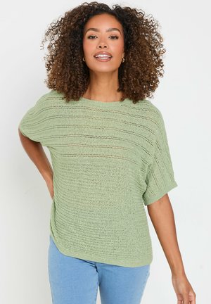 Groen gebreid topje met een ontspannen fit, korte mouwen en een gestructureerd patroon. Gecombineerd met lichtblauwe spijkerbroeken.